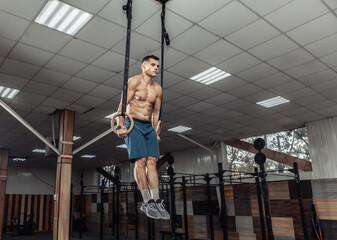 Fototapeta na wymiar Muscular male gymnast exercising on gymnastic rings in a modern health club. Healthy lifestyle concept