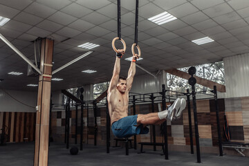Muscular male gymnast exercising on gymnastic rings in a modern health club. Healthy lifestyle concept