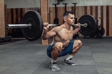 Fototapeta na wymiar Young muscular male bodybuilder doing squats with a barbell on his shoulders in a modern health club. Bodybuilding and Fitness