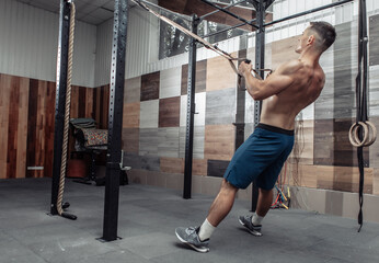 Muscular man exercising with the trx resistance system in a modern cross-fit club. Functional training