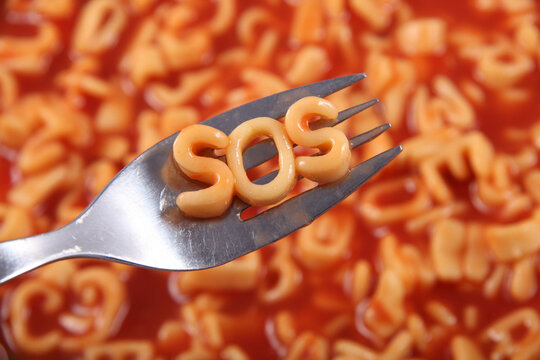 Spaghetti letter spelling the word SOS standing for Save Our Souls, with the letters held up on a fork, behind is the red tomato sauce.