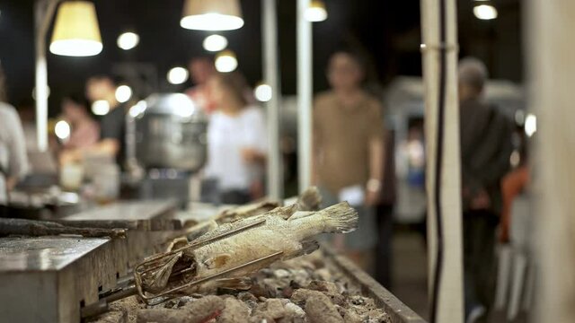 Handheld shot of frying fish on a skewers, street food market in Singapore. Rows of small fishes being fried spinning on skewers at street food local market