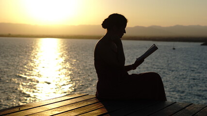silhouette of young girl reading near the sea