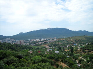Obraz premium A village with houses and gardens in a picturesque valley surrounded by hills. Trees grow on the hillsides. Clouds float across the sky.