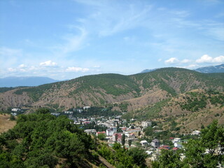 Obraz premium A village with houses and gardens in a picturesque valley surrounded by hills. Trees grow on the hillsides. Clouds float across the sky.