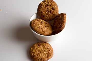 Home made biscuit with peanuts on top, biscuits stacked inside a white cup with white background and light shadows and sugar crystals