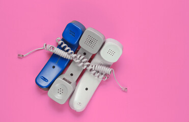 Three office phone tubes wrapped in cable on pink studio background. Call center, hotline concept
