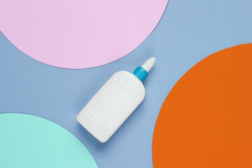 Bottle of glue on blue paper background with circles. Top view