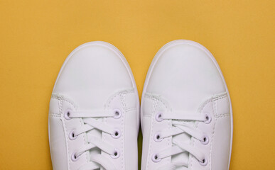 Stylish white sneakers on yellow paper background. Minimalistic fashion concept. Top view