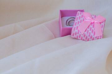 Pink box with wedding rings on a white linen cloth. Concept love, wedding, romance, Valentine's Day. Space for writing.