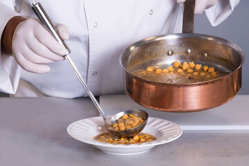 view of chickpea stew being served by a male chef using a ladle on an out of focus background