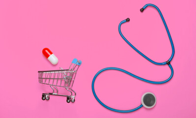 The concept of healing. Flat lay composition. Stethoscope, shopping trolley with capsule on pink...