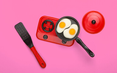 Miniature toy frying pan with fried eggs on stove. Pink background. Top view. Minimalism. Studio shot