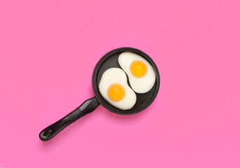 Miniature toy frying pan with fried eggs on pink background. Top view. Minimalism food concept, breakfast. Studio shot