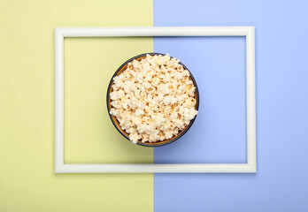 Bowl of popcorn on yellow blue pastel background with white frame. Leisure and entertainment concept. Top view