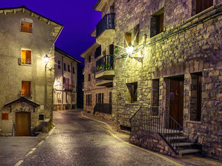 Mountain village street at night. Architecture of stone houses, balconies with flowers and illuminated alleys. Torla Ordesa.

