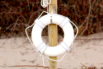 Life preserver ring on beach, hanging on a wooden post. Sand and brush in the background.