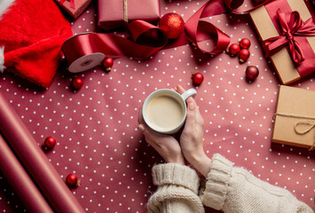 Woman hands hold cup of coffee near gifts on wrapping paper