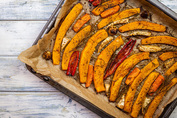Roasted pumpkin slices in baking tray on white wooden table