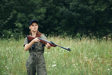 Woman on nature gun in hand fresh air traveler hunting green overalls 