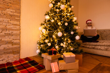 woman with laptop on the background of a Christmas tree accepts online congratulations merry christmas