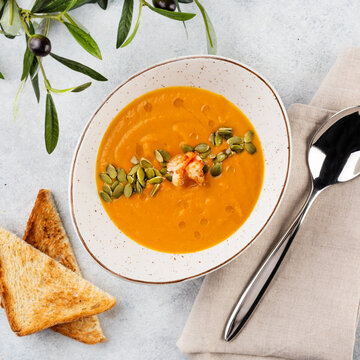 Tasty appetizing pumpkin creamy soup decorated with prawn and pampkin seeds on white background. Top View.