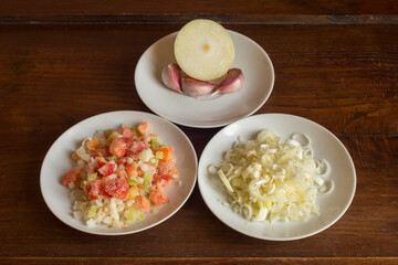 Natural food ingredients and vegetables on white plates on a chestnut wooden table. Sauteed vegetables, garlic, and leek. Preparation of cooked dishes.