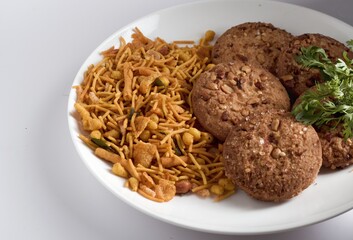 plate with Indian Mixture and home made biscuits with coriander leaves for evening snakes with coffee or tea in white background. food for leisure. tasty home made indian cookies, mixture background