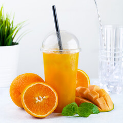 Orange and mango fruit healthy fresh drink in plastic cups on bright background. Colorful diet...