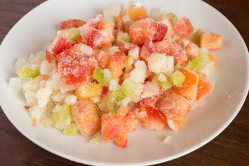 Sauteed vegetables, garlic, and leek on a white plate on a chestnut wooden table. Preparation of recipes with natural food ingredients and vegetables.