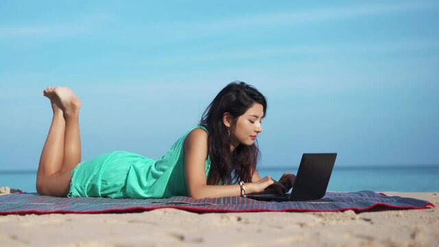 Portrait of pretty woman on beach in front of laptop. Girl freelancer working on computer surrounded by beautiful tropical landscape. Concept of travel.