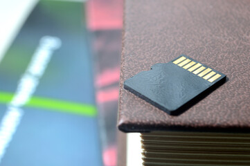 micro sd card lies on top of a paper book, golden contacts at the top. close-up.