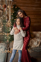 Young mother with two little daughters in pajamas decorate a New Year's tree in the cozy room with with big light window