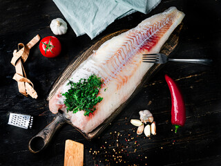 Fresh codfish fillet with cooking ingredients on a wooden cutting board. Top view. 