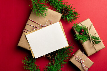 Christmas greeting card mockup with decorated gift boxes and green pine tree branches on red paper background