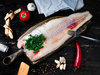 Fresh codfish fillet with cooking ingredients on a wooden cutting board. Top view. 