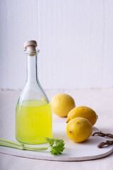 Traditional Italian liqueur Limoncello. Glass bottle with homemade Limoncello liqueur, plate with lemons and celery.
