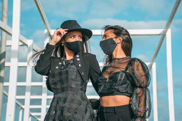 Two young women dressed in black clothing and face masks.