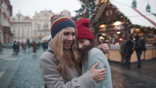 Two girls fooling around in middle of christmas fare. Young girls laughing and joking, having good time in a center of square in european town. Friends being close and travel together during holidays.
