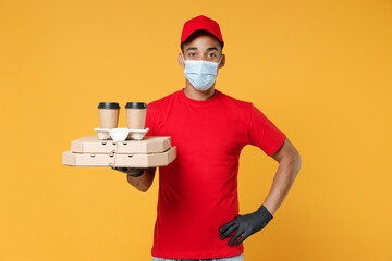 Delivery employee african man in red cap blank print t-shirt face mask gloves work courier service on quarantine coronavirus covid-19 virus hold cardboard pizza flatbox isolated on yellow background.