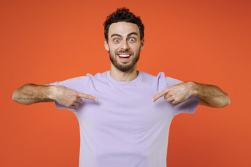 Cheerful excited young bearded man 20s wearing basic casual violet t-shirt standing pointing index fingers on himself looking camera isolated on bright orange color wall background studio portrait.