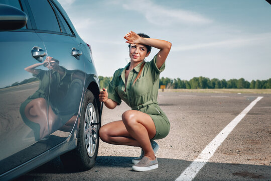 young fit girl is tired to fix a wheel of her broken car by socket wrench under the hot sun