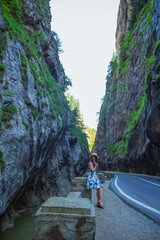 Elegant woman dressed in white blue dress and straw hat sitting near mountain river and dangerous road in Bicaz Canyon. Bicaz Key, geological wonders of nature, Transylvania, Romania.