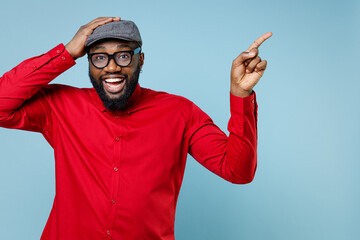 Excited young bearded african american man 20s in red shirt eyeglasses cap put hand on head...