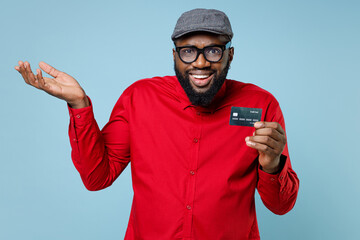 Perplexed young bearded african american man 20s wearing casual red shirt eyeglasses cap standing...