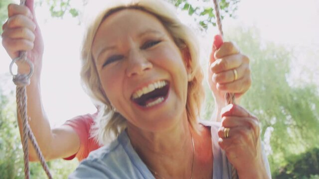 Close up of retired senior couple having fun with man pushing woman on garden swing - shot in slow motion