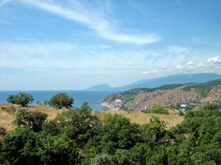 Obraz premium View of the village with houses and gardens in a picturesque valley by the sea. Trees grow on the hillsides. Clouds float across the sky.