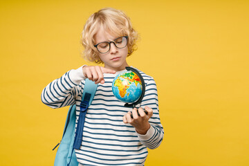 Little male kid teen boy 10s years old in striped sweatshirt eyeglasses backpack point index finger on world Earth globe isolated on yellow color background, child studio portrait. Education concept.