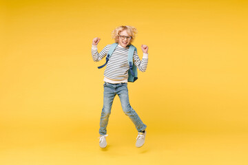 Full length of happy male boy 10s years old wearing striped sweatshirt eyeglasses backpack jumping doing winner gesture isolated on yellow color background child studio portrait. Education concept.
