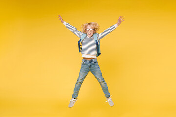 Fototapeta na wymiar Full length of excited male boy 10s years old in striped sweatshirt eyeglasses backpack jumping spreading hands and legs isolated on yellow color background child studio portrait. Education concept.
